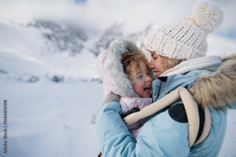 Mother standing in the middle of snowy landscape with daughter in baby carrier. Mom and girl enjoying winter holiday in the mountains. Mother standing in the middle of snowy landscape with daughter in baby carrier. Mom and girl enjoying winter holiday in the mountains.