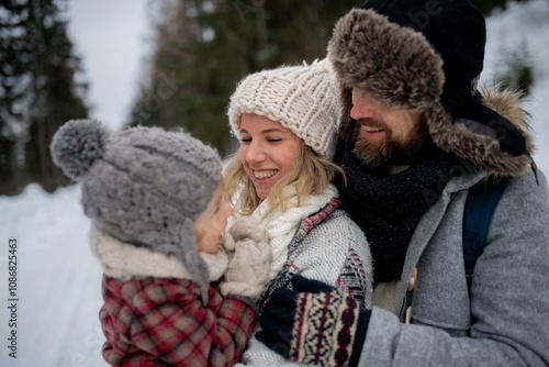 Young family is enjoying winter holiday in the mountains, standing in the middle of snowy forest.