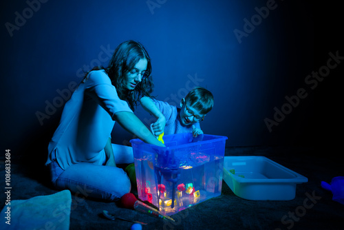 Child and therapist in sensory stimulating room, black snoezelen. Autistic child playing with therapist during occupational therapy session. photo