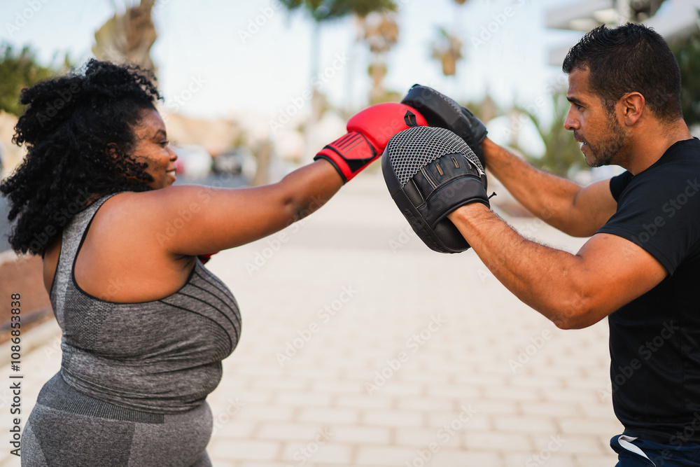 African curvy girl doing boxing workout session outdoor with her personal trainer - Sport and healthy lifestyle concept - Focus on man ear African curvy girl doing boxing workout session outdoor with her personal trainer - Sport and healthy lifestyle concept - Focus on man ear