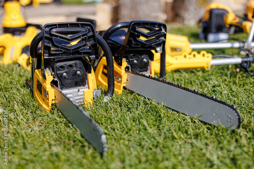 A Trio of Power: Gleaming Chainsaws Resting on Lush Green Grass, Ready to Conquer Nature's Challenges. Their Metallic Blades Reflecting the Serenity of the Natural World Around Them.