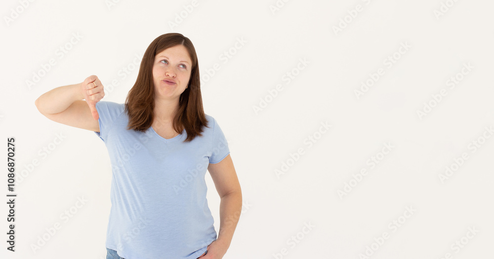 Young sad displeased unhappy woman wear blue t-shirt showing thumb down dislike gesture isolated on white background studio portrait. People lifestyle concept Young sad displeased unhappy woman wear blue t-shirt showing thumb down dislike gesture isolated on white background studio portrait. People lifestyle concept