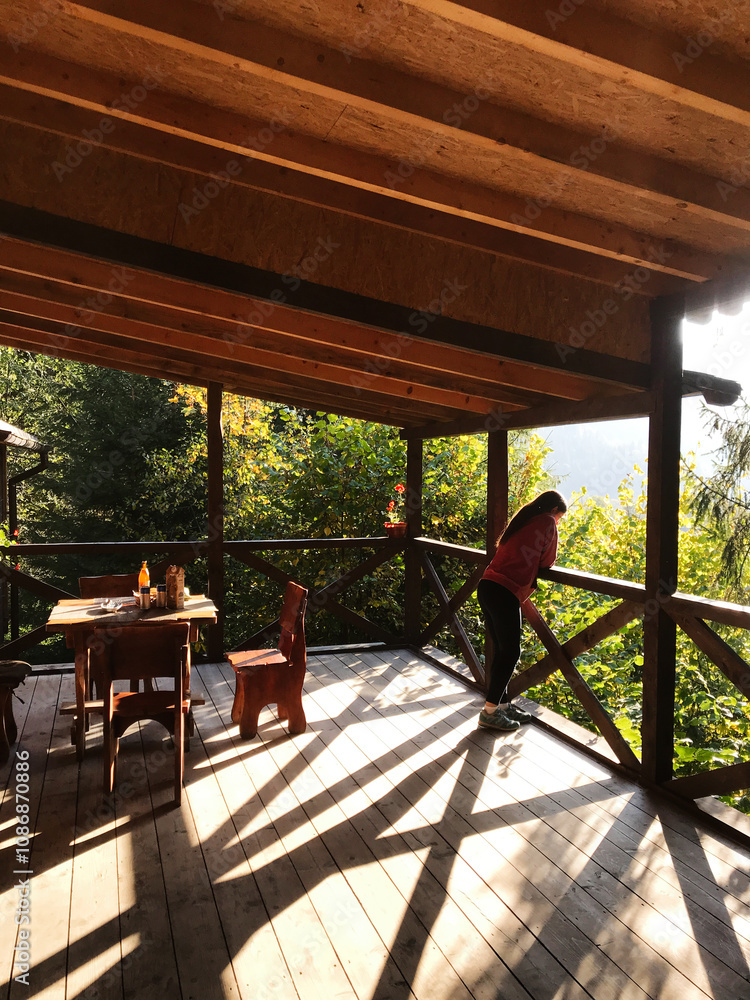 Fototapeta premium Woman enjoying serene forest view from wooden cabin terrace