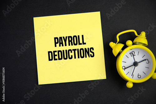 Yellow memo paper with the word Payroll Deductions beside alarm clock. Business Concept