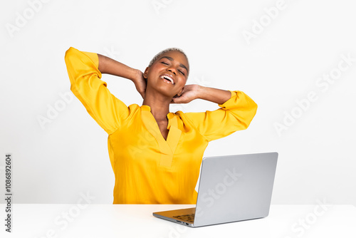 Happy young freelancer sitting with hands behind head and laptop at desk against white background photo