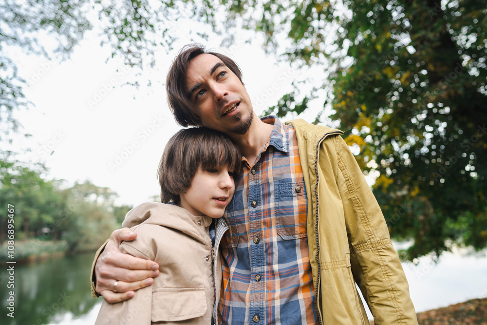 Father hugging teenage boy by lake in autumn park Father hugging teenage boy by lake in autumn park