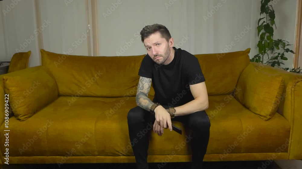 Man watching straight into the camera and pointing tv remote forward to switch channels on the tv that appears to be in front of him. Movement is in slow motion and the man has full sleeve tattoos. Man watching straight into the camera and pointing tv remote forward to switch channels on the tv that appears to be in front of him. Movement is in slow motion and the man has full sleeve tattoos.