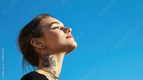 A beautiful young woman with a tattoo on her neck and a piercing in her , looking up at the cl blue sky. photo