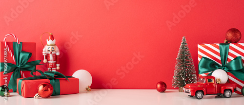 A vibrant Christmas setup featuring wrapped gifts, a miniature tree, and ornaments against a red backdrop. Includes a nutcracker and toy truck for a classic holiday touch photo