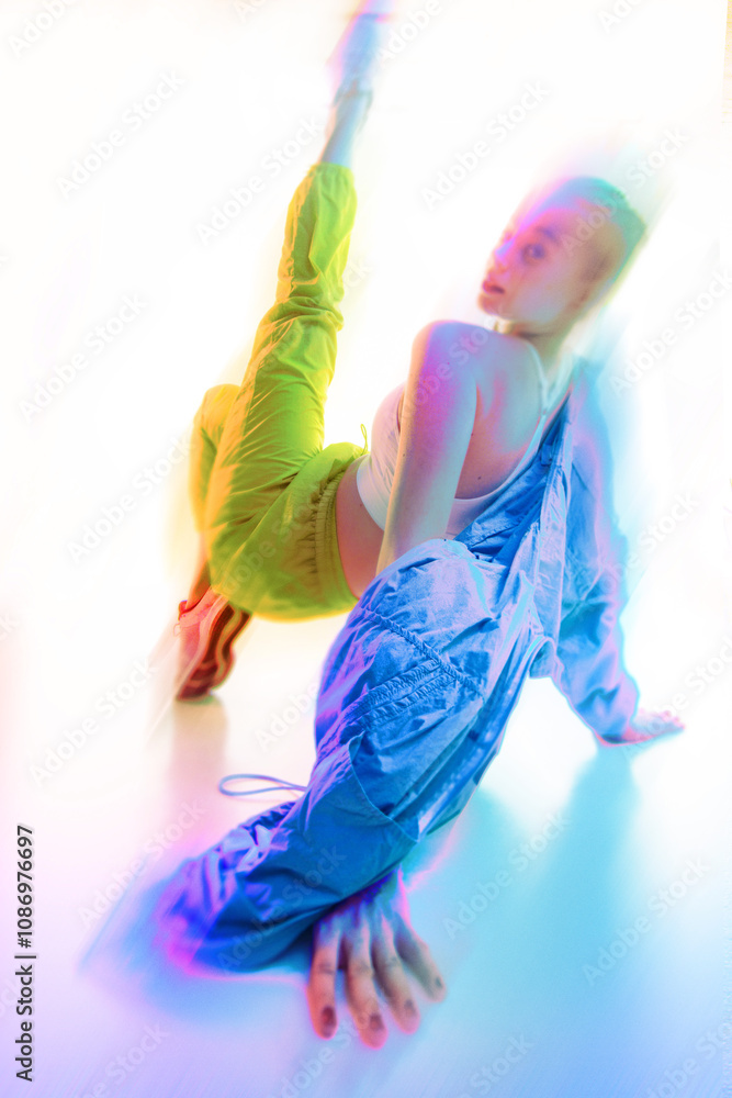 Obraz premium Contemporary art collage. Woman stretching dynamically on floor, wearing vibrant athletic clothing, surrounded by glowing neon light effects. Concept of fashion, style, lifestyle. Motion blur effect.