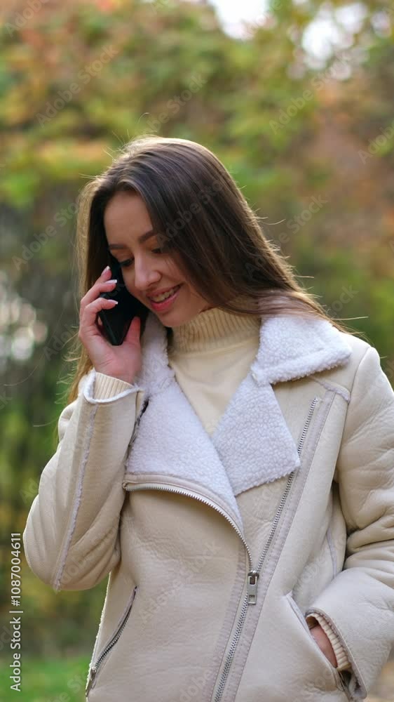 Beautiful dark-haired lady in white jacket walking slowly by the autumn wood. Attractive woman speaks on the phone continuing her walk. Vertical video Beautiful dark-haired lady in white jacket walking slowly by the autumn wood. Attractive woman speaks on the phone continuing her walk. Vertical video
