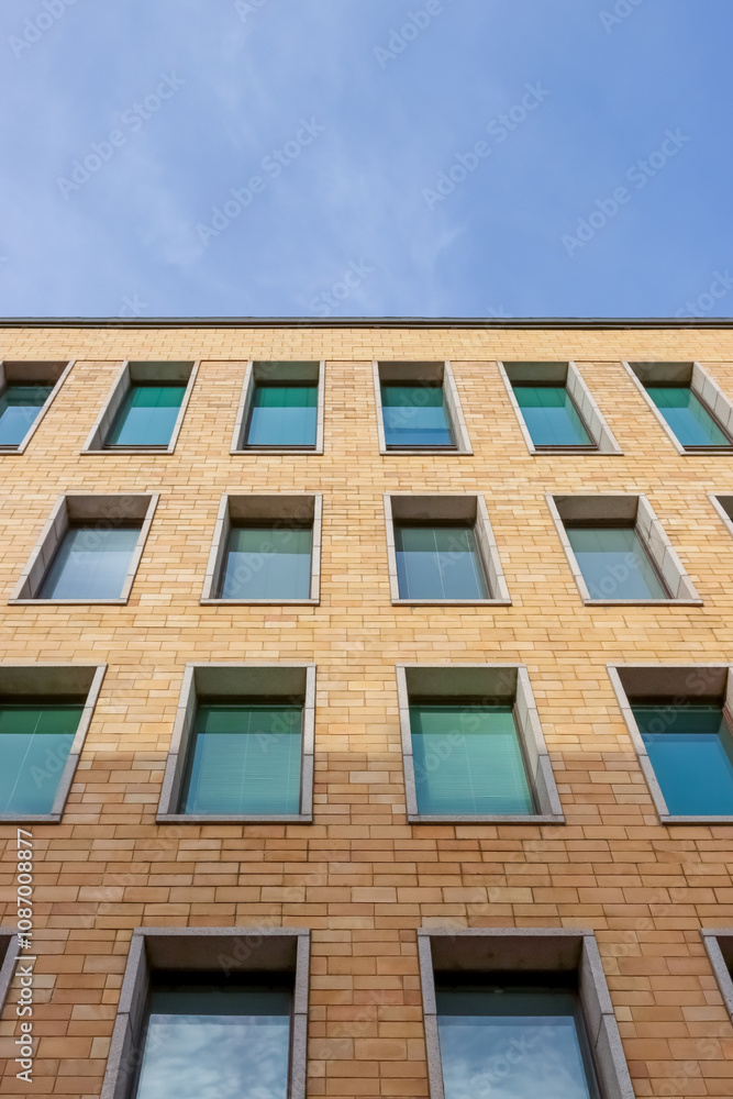 Close-up view of a modern building facade with symmetrical brickwork and multiple windows, showcasing urban architecture and design. Empty space for text. Close-up view of a modern building facade with symmetrical brickwork and multiple windows, showcasing urban architecture and design. Empty space for text.