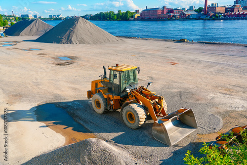 Tractor with bucket heaps of gravel, crushed stone, pebbles in the port, a large storage of bulk minerals and stones on the shore of the port in the city photo