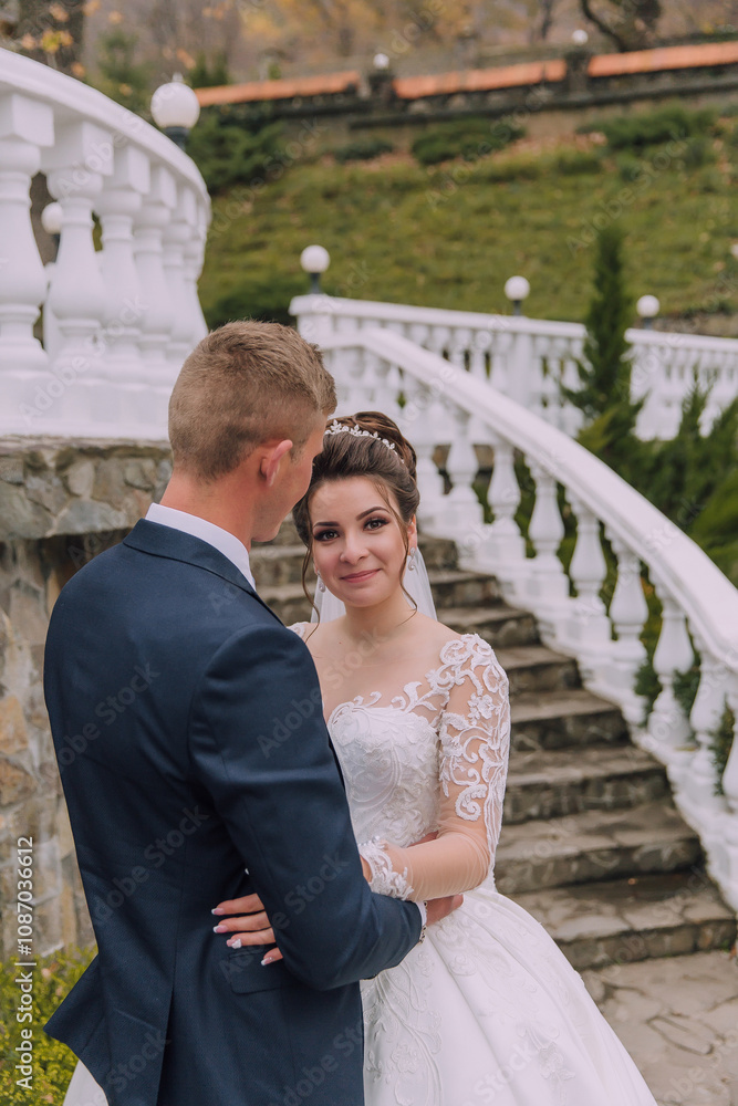 A bride and groom are standing on a staircase, the bride is wearing a white dress and the groom is wearing a blue suit A bride and groom are standing on a staircase, the bride is wearing a white dress and the groom is wearing a blue suit