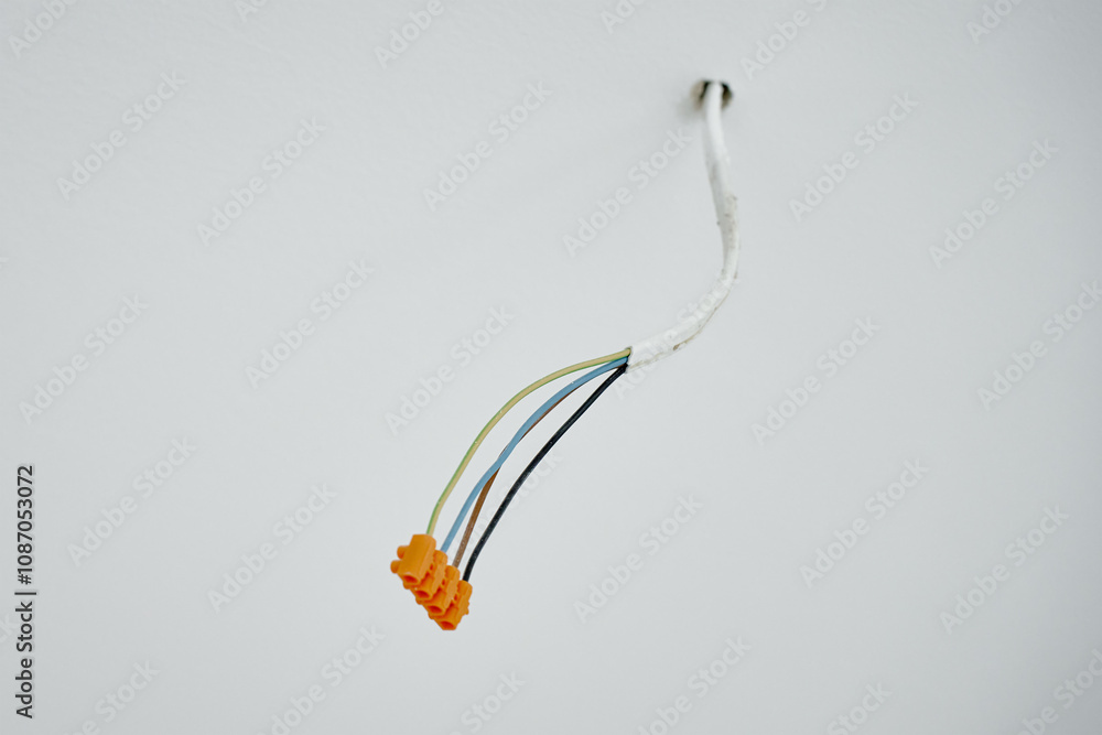 Close-up of electrical wires extending from white wall. Electrical work during apartment renovation. Electricity cable in new apartment Close-up of electrical wires extending from white wall. Electrical work during apartment renovation. Electricity cable in new apartment