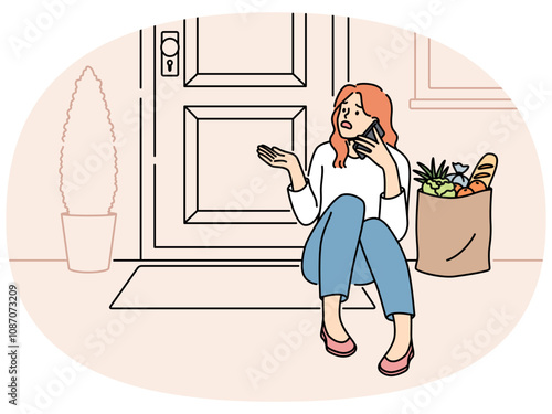 Embarrassed woman sits on threshold near door with jammed lock and cannot get into house, makes phone call. Puzzled girl with bag of groceries, calling specialist because of loss of key to door