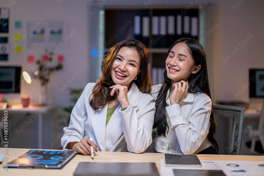 Two women are smiling and laughing at a desk with a computer and a tablet Two women are smiling and laughing at a desk with a computer and a tablet