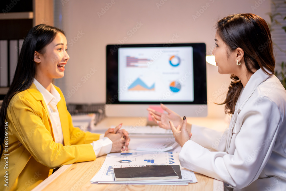 Two women are sitting at a desk with a computer monitor in front of them Two women are sitting at a desk with a computer monitor in front of them