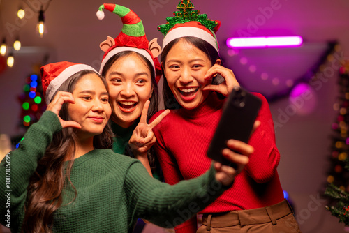 Three women are posing for a picture with a cell phone, wearing Santa hats