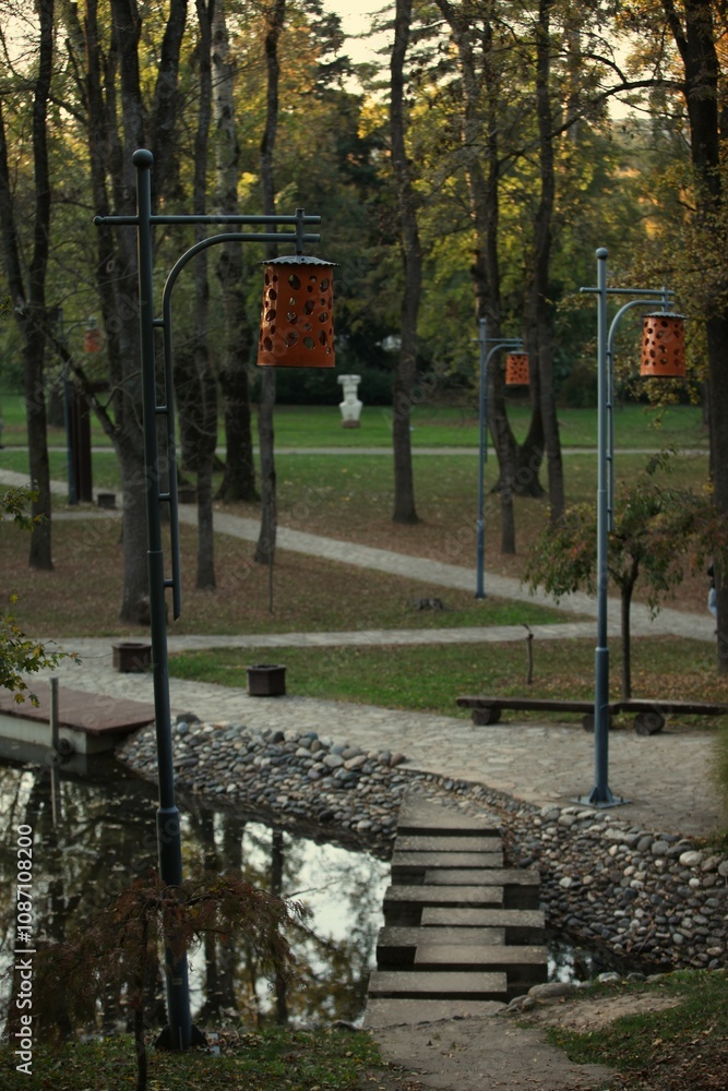 Obraz premium A stone path across a lake in a park, orange lamps on the side