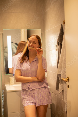 Smiling young woman brushing teeth in bathroom. Keeping her smile. photo