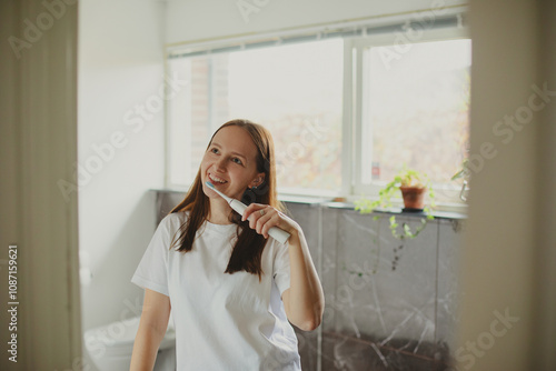 Smiling young woman brushing teeth in bathroom. Keeping her smile. photo