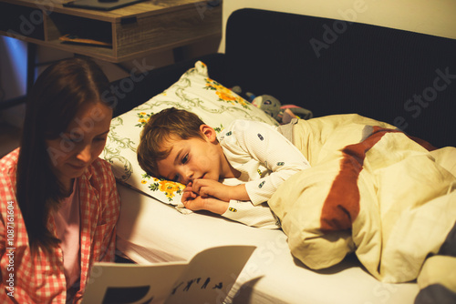 A loving mother reads a bedtime story to her son, creating a warm and comforting nighttime ritual photo