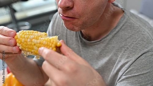 Close-up of Caucasian man eating yellow juicy corn cob eats with appetite in kitchen enjoy vegetarian dishes, organic healthy food