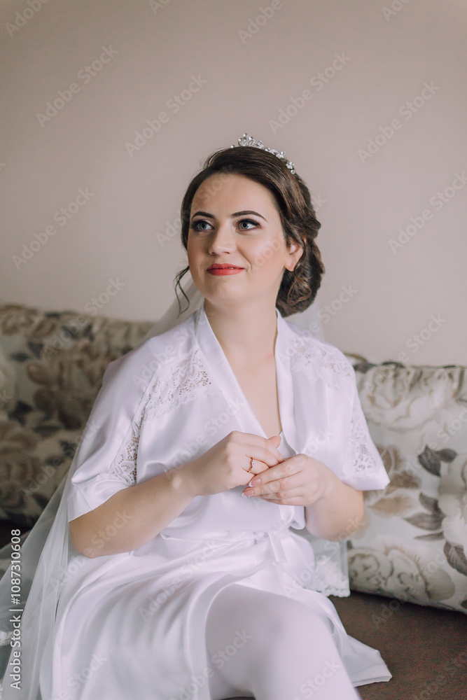 A woman in a white robe sits on a couch. She is wearing a white veil and a ring on her finger A woman in a white robe sits on a couch. She is wearing a white veil and a ring on her finger