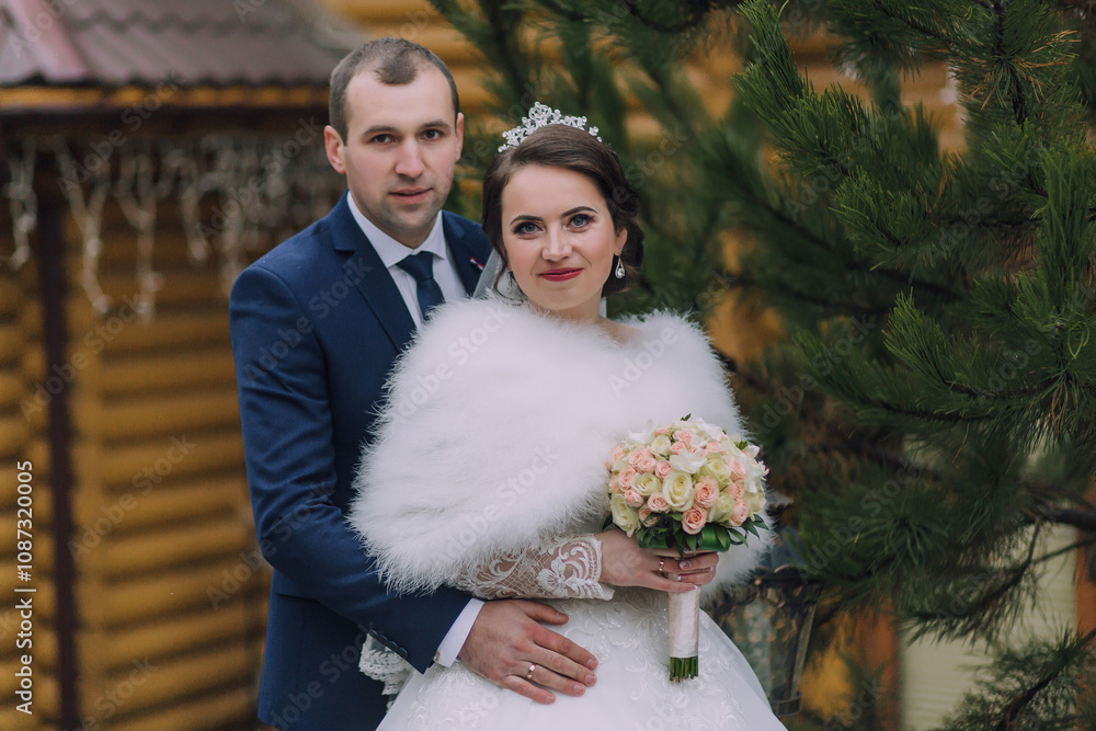 A bride and groom are posing for a picture in front of a house. The bride is wearing a fur coat and holding a bouquet of flowers A bride and groom are posing for a picture in front of a house. The bride is wearing a fur coat and holding a bouquet of flowers