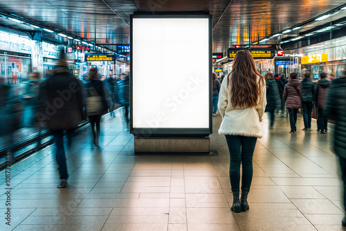 Femme de dos regardant un panneau blanc dans une gare
