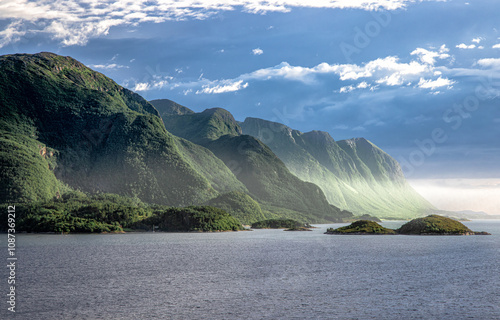 Eine begrünte Bergformation im Fjord von Molde. Dunst sammelt das Licht der tiefen Sonne am Fuße der extrem steilen Bergflanken. Schöne Licht Schattenspiel. photo