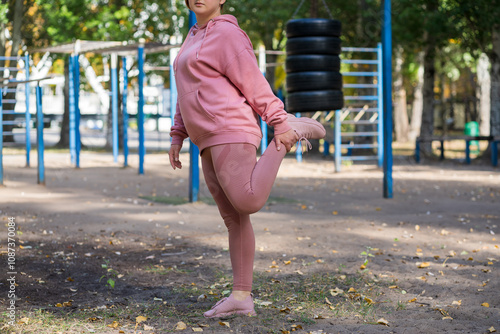 Obese woman in pink leggings with fat legs exercising on sports ground, outdoor weight loss exercise