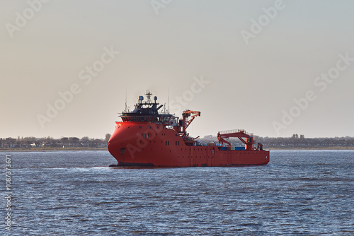 Fotografie Red offshore support vessel sailing in port on a bright day.