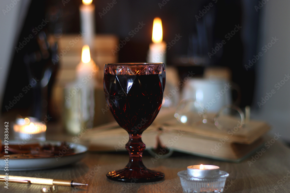 Books, lit candles, red wine, snacks and various deocration on the table. Dark academia or Halloween concept. Selective focus. Books, lit candles, red wine, snacks and various deocration on the table. Dark academia or Halloween concept. Selective focus.