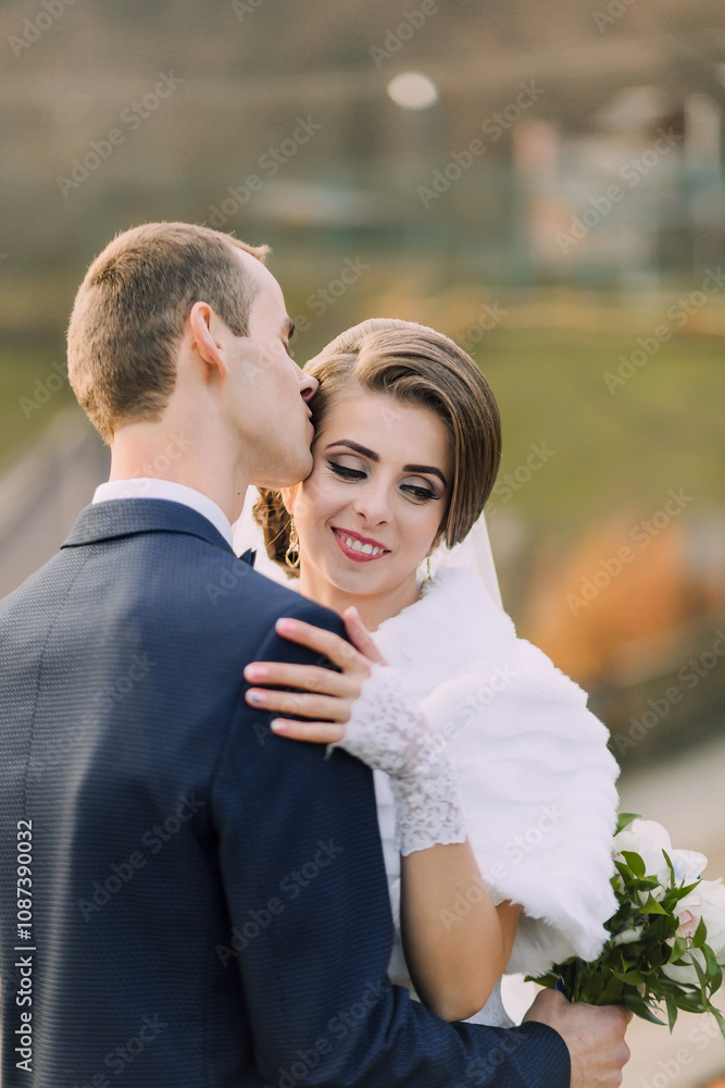 A bride and groom are hugging each other, with the bride wearing a white fur stole. The man is kissing the woman's neck A bride and groom are hugging each other, with the bride wearing a white fur stole. The man is kissing the woman's neck