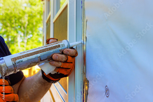 In residential construction project, worker wearing protective gloves carefully applies caulk to edges of window frame to ensure tight seal against air leaks. photo