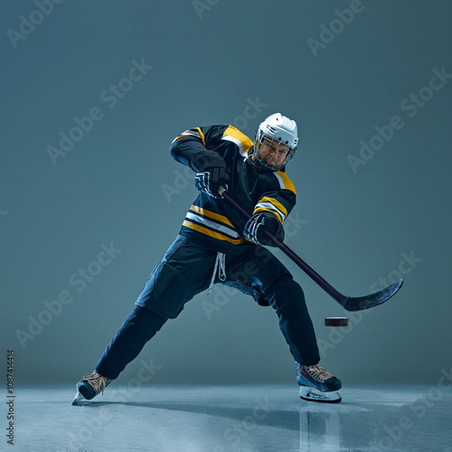 Photography Hockey player wearing black and yellow uniform, captured in mid-action with stick to hit puck, against studio background