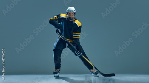 Canvas Print Determined man, hockey player in mid-skate, controlling puck with stick, wearing full black and yellow uniform and helmet, playing