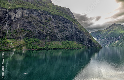 Steil stürzt ein Wasserfall an einer Felsformation im Geiranger Fjord in Norwegen in das türkisblaue Meer