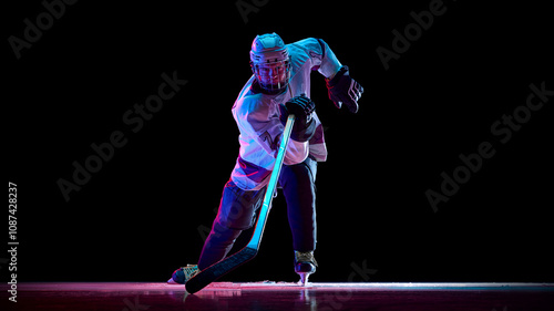 Photography Dynamic image of man, hockey player in motion with stick, training, playing intense game against black studio background in neon light