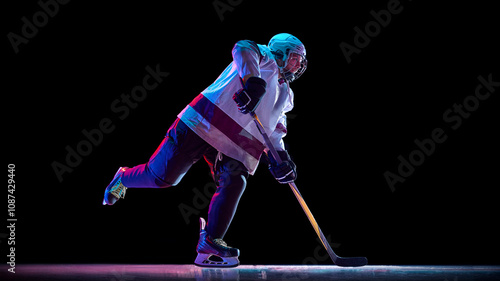 Canvas Print Side view dynamic image of man, hockey player in motion with stick, training, playing intense game against black studio background in neon light