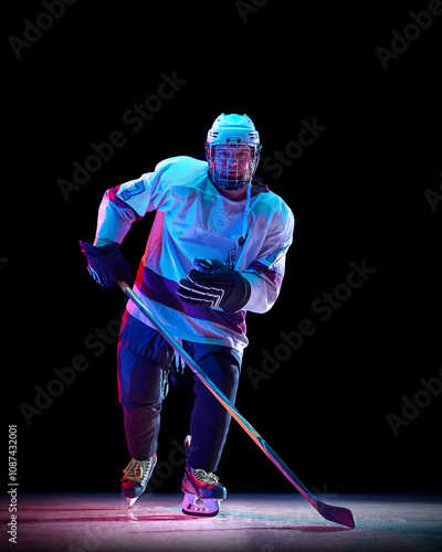 Photography Dynamic image of competitive men's, hockey player in white sportswear in motion on ring with stick, against black studio background in neon light