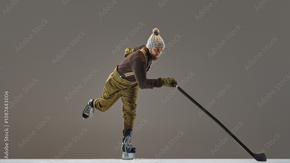 Obraz premium Winter sports. Man wearing knitted sweater, hat and pants with suspenders, ice skating with stick, playing hockey. Concept of sport, game, tournament, action, competition