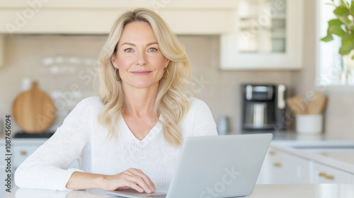 Smiling woman works happily from home on her laptop at a cozy kitchen table, exuding confidence and comfort in a modern interior setting