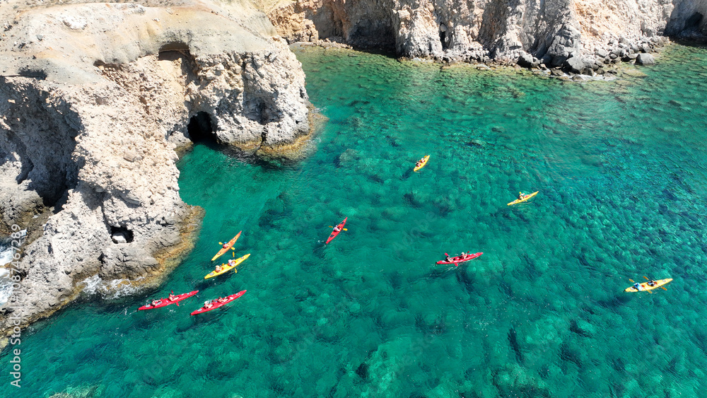Aerial drone photo of team of canoeing athletes rowing in tropical exotic caves of Tsigrado beach in Milos, Cyclades, Greece