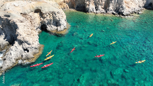 Aerial drone photo of team of canoeing athletes rowing in tropical exotic caves of Tsigrado beach in Milos, Cyclades, Greece