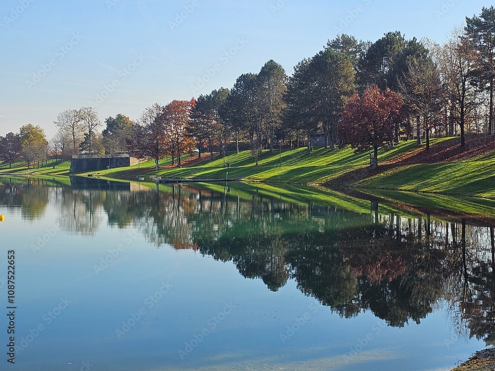 Wunderschöne Spiegelung von Böschung, Bäumen und Rasen in See im Herbst