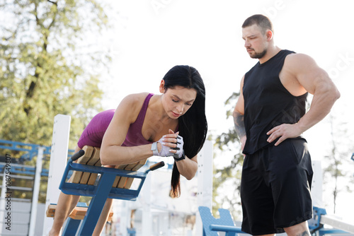 A trainer helps a young woman to perform back extension on a simulator in an open-air gym. photo