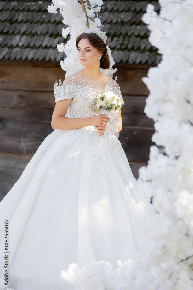 A woman in a white dress is holding a bouquet of flowers. She is standing in front of a white archway A woman in a white dress is holding a bouquet of flowers. She is standing in front of a white archway
